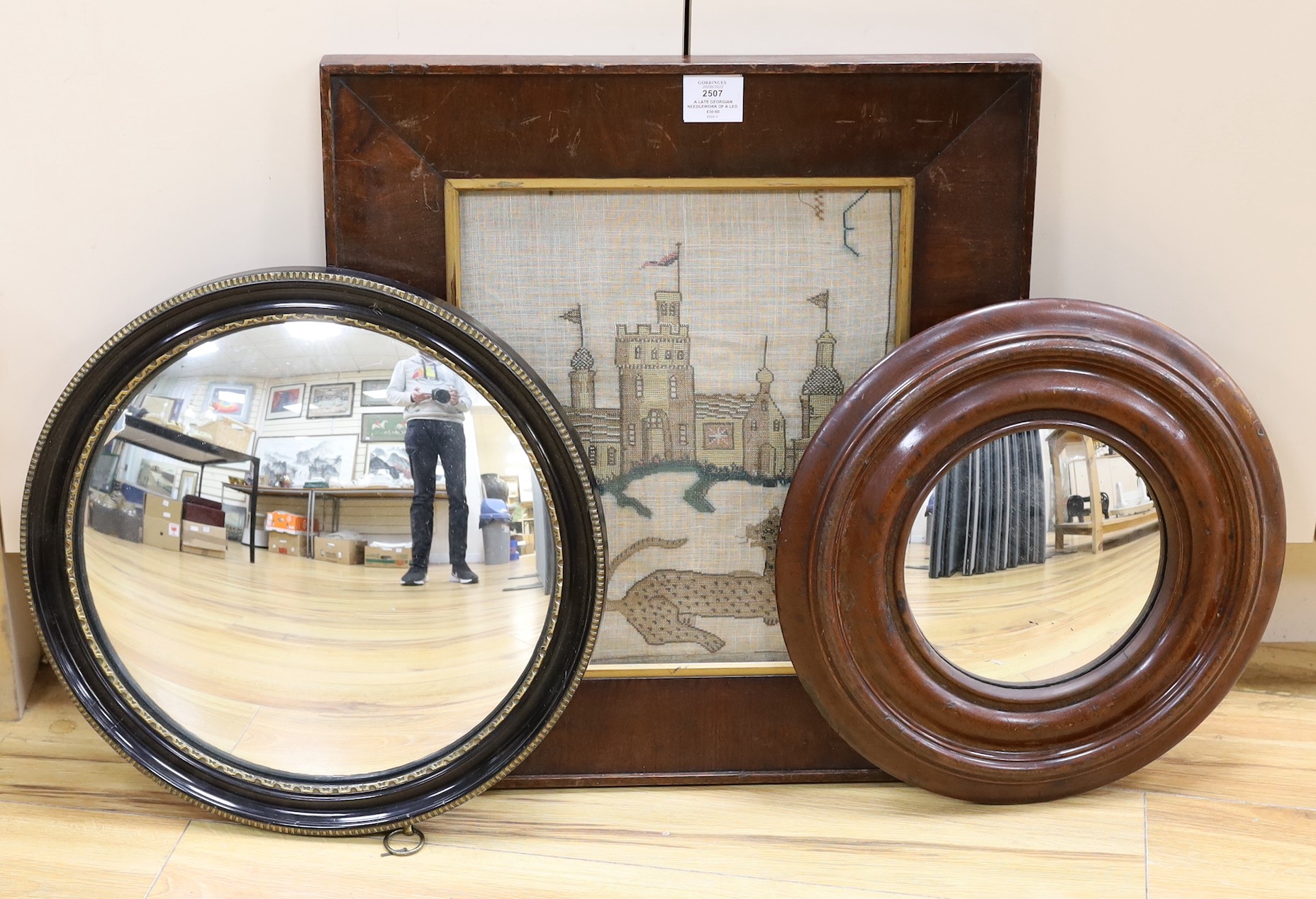 A late Georgian needlework of a leopard and castle , together with a turned wooden framed convex mirror and a similar ebony and gilt framed convex mirror, needlework 31 cms x 36 cms